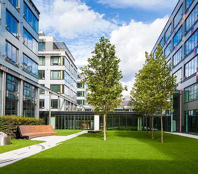 Hausbetreuung - Moderner Büropark mit grünem Rasen, Bäumen und Bank